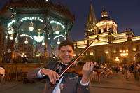 Violinist Sergio Caratachea Alvarez of the Mariachi Internacional de Guadalajara on Plaza de Armas with the kiosko and cathedral lit up in the background. Guadalajara, Jalisco, Mexico